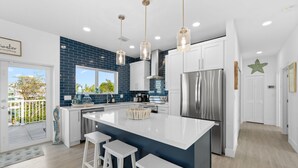 A modern kitchen with a central island, white bar stools, stainless steel appliances, and a blue backsplash. - Blue Pearl Waterfront Oasis w Pool 70 Dock (Marathon)