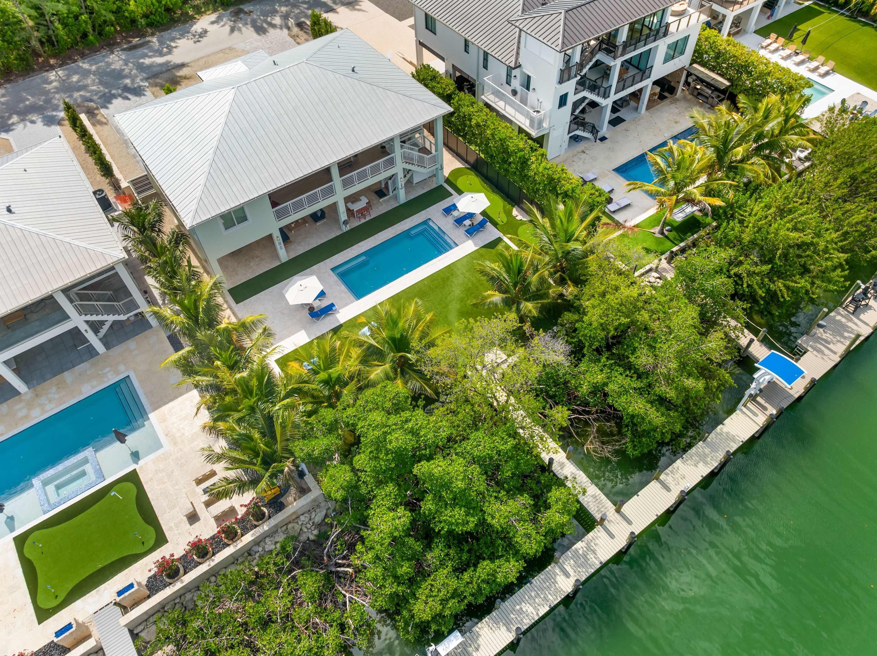 A multi-story resort with a swimming pool, outdoor seating, and a dock extending into a body of water.