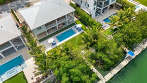 A multi-story resort with a swimming pool, outdoor seating, and a dock extending into a body of water.