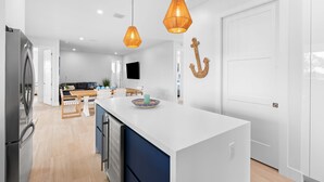 A modern kitchen with a central island, pendant lights, and a white door.
