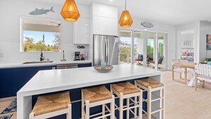 A modern kitchen with a large island, bar stools, and hanging pendant lights.