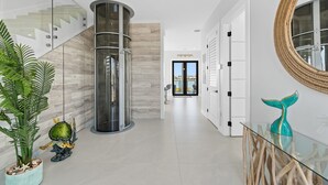 A modern interior with a glass staircase, a central column, a view through a door, and a glass table with a decorative item. - Luxury Seaside Escape Pool Dock Scenic Views (Marathon)