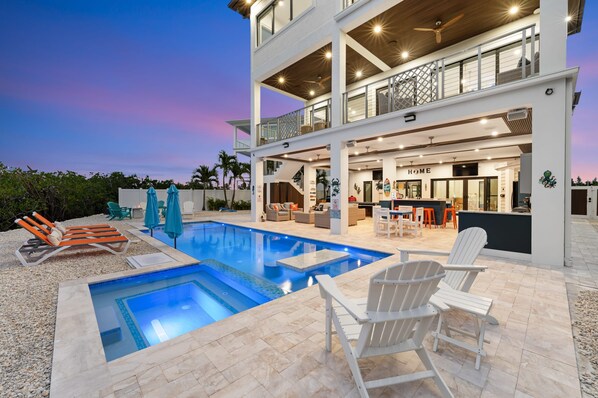 A two-story house with a swimming pool, outdoor seating, and a bar area.