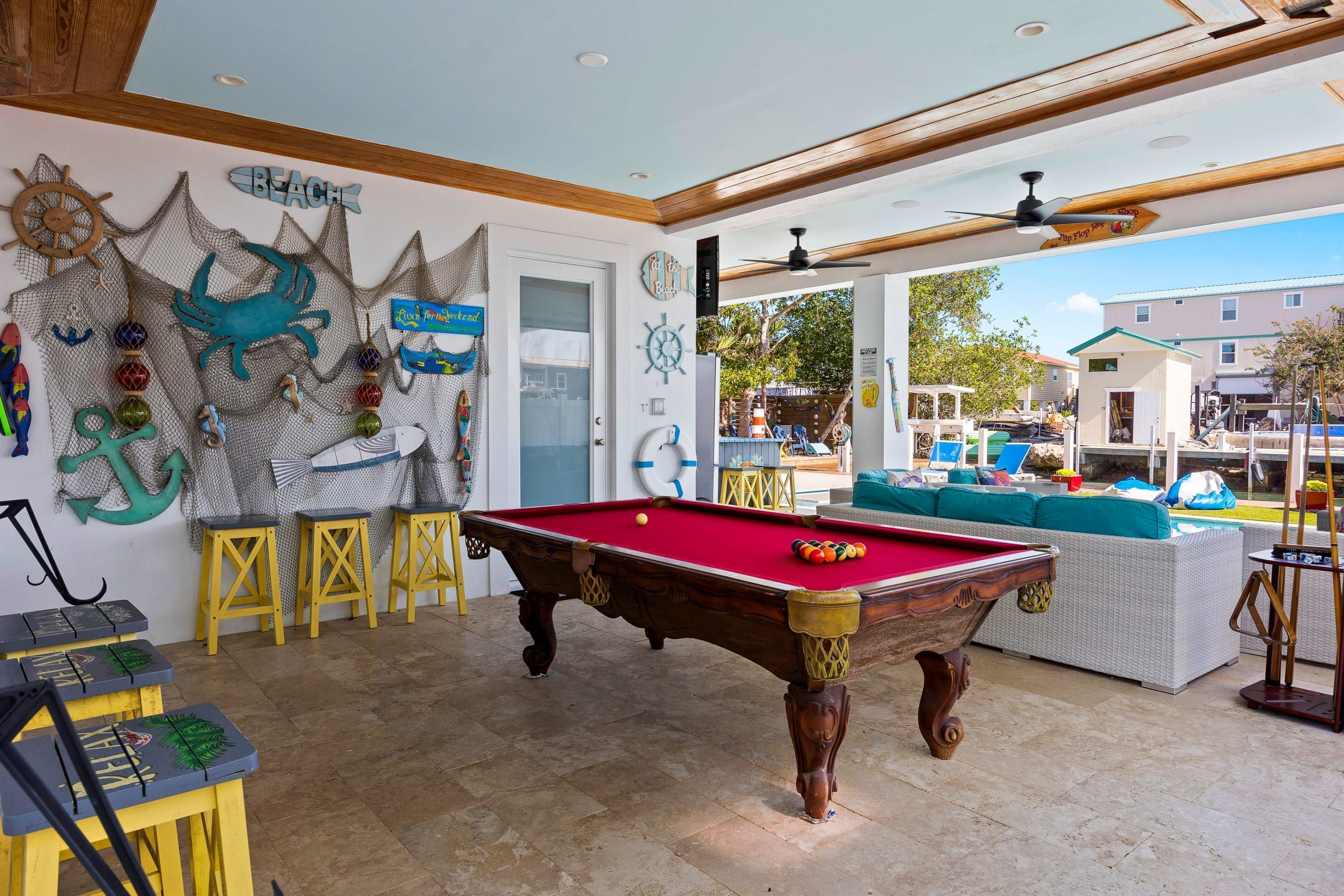 Une table de billard dans une pièce dotée d’un ventilateur de plafond, d’une porte et offrant une vue sur l’extérieur.