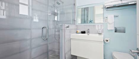 A modern bathroom with a glass-enclosed shower, a white sink, and a toilet.