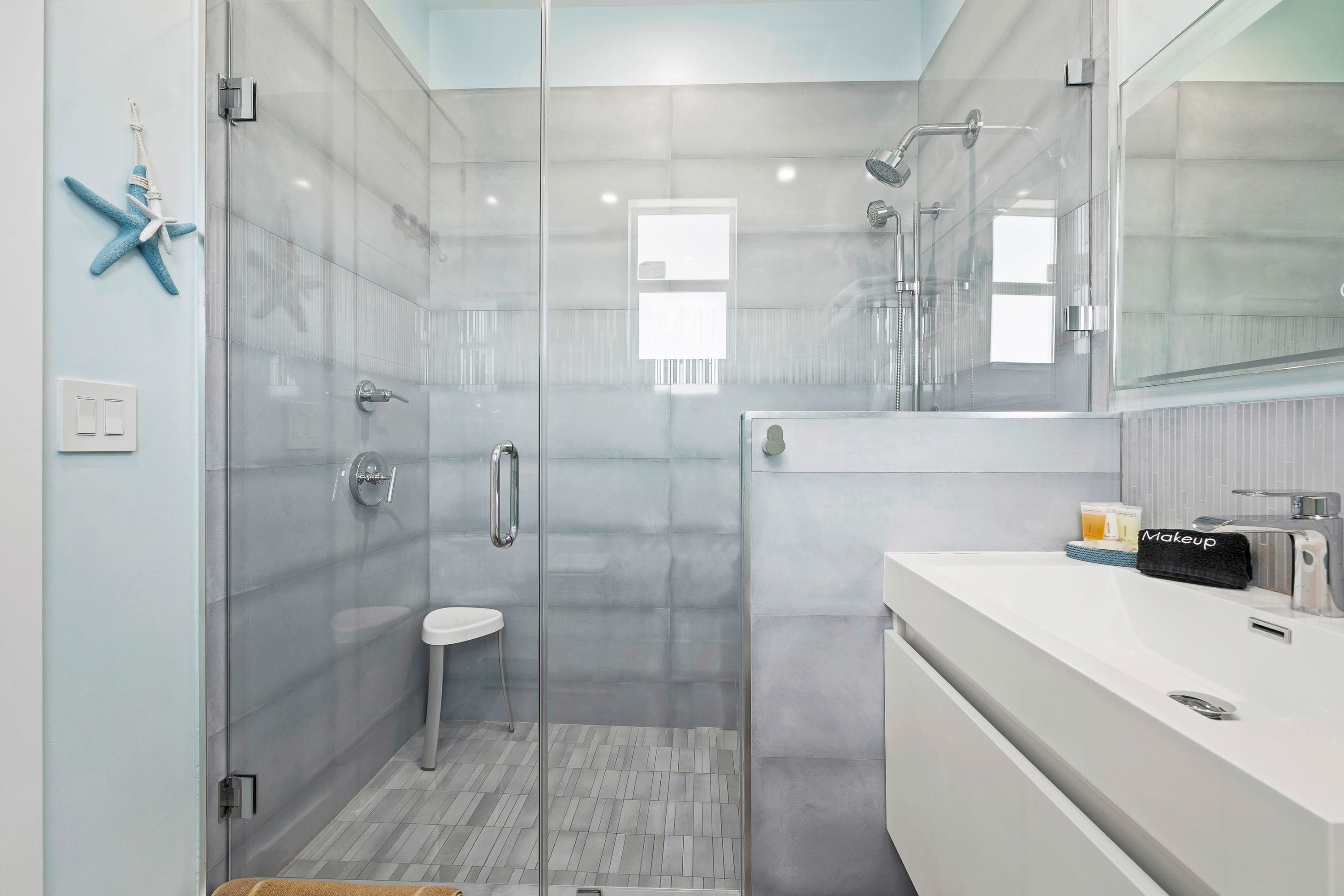 Un baño moderno con ducha de vidrio, lavamanos blanco y un espejo grande.