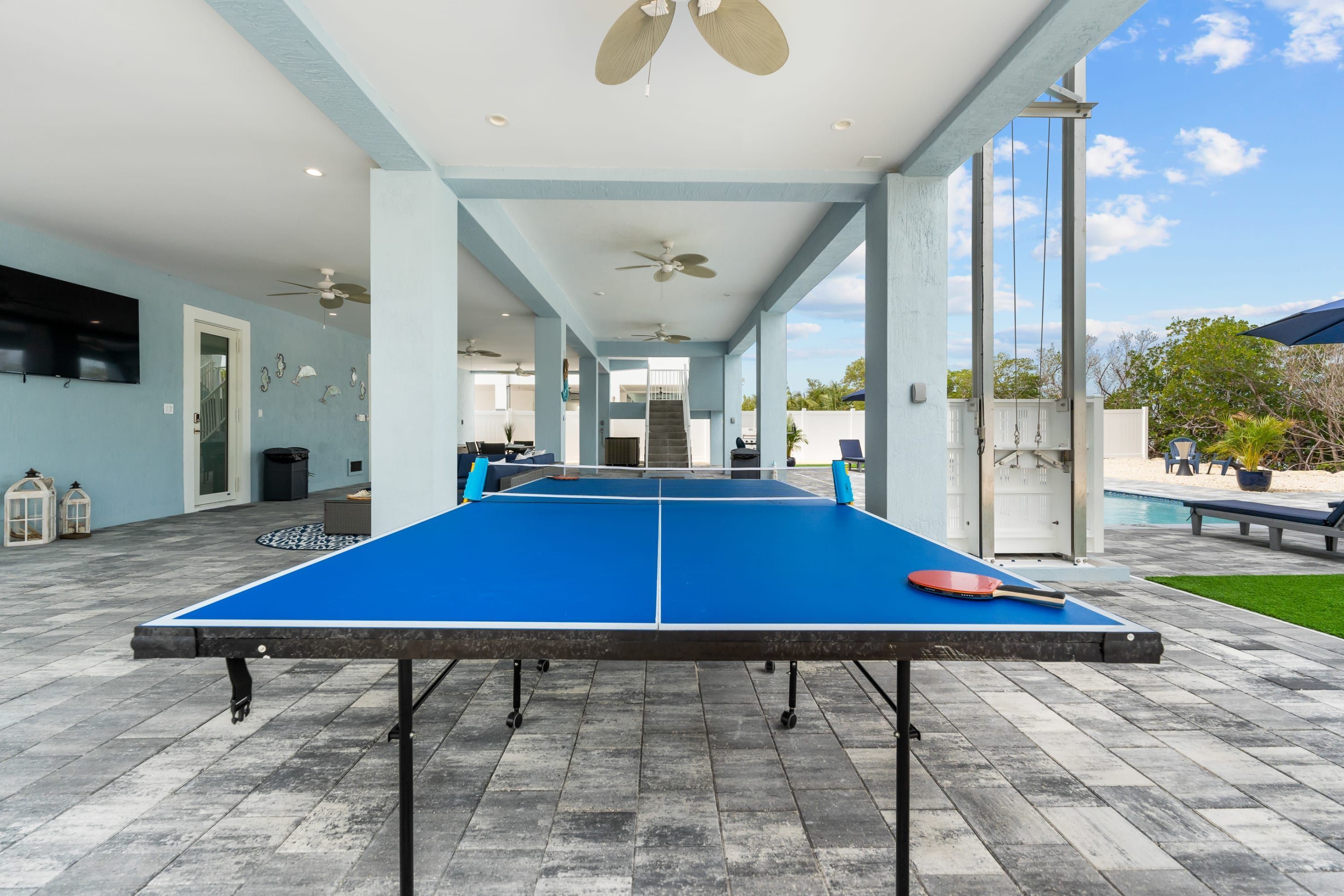 A ping pong table with a paddle, set up on a patio with a pool in the background.