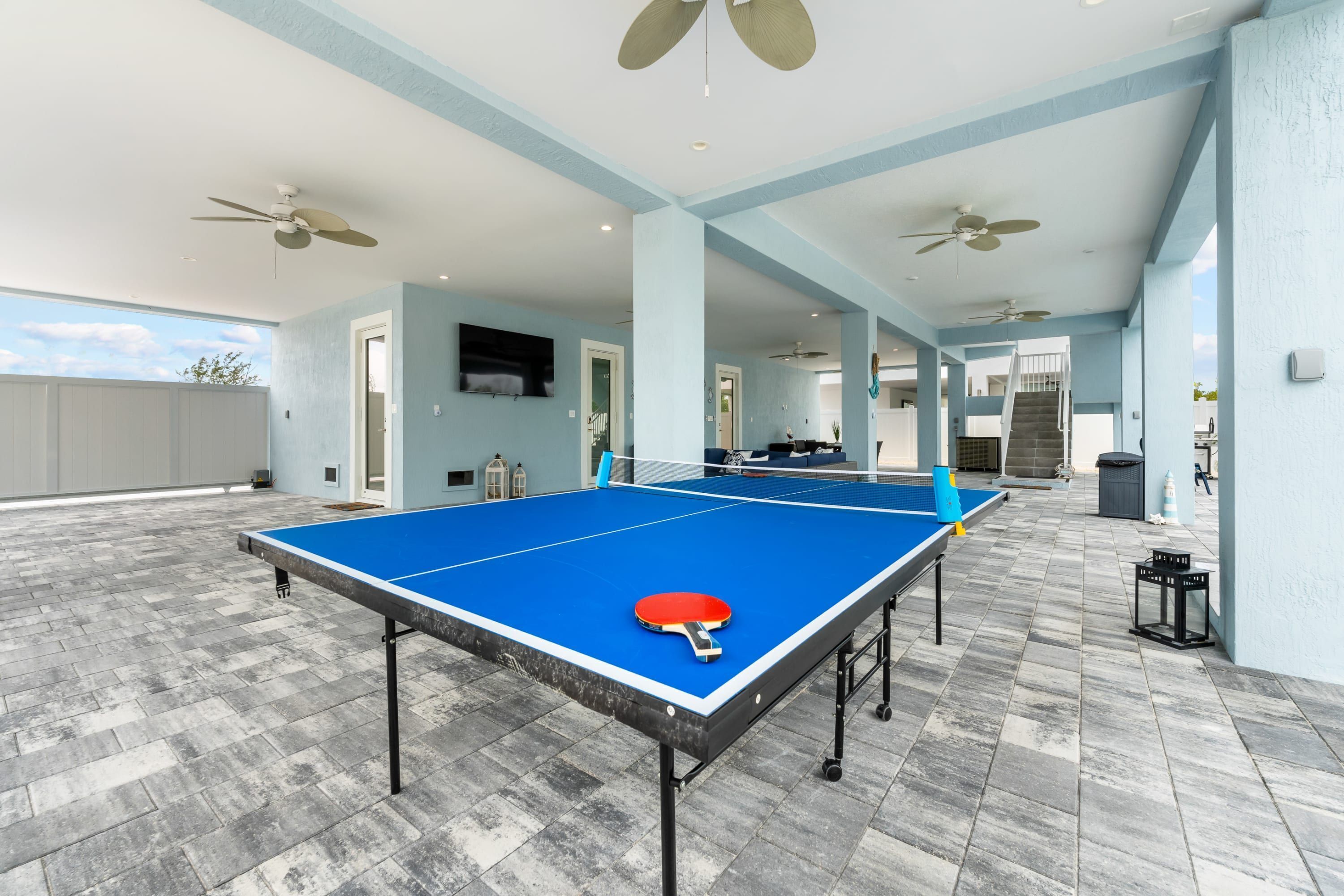 Un'ampia area interna con tavolo da ping pong, ventilatori a soffitto e vista sull'esterno.