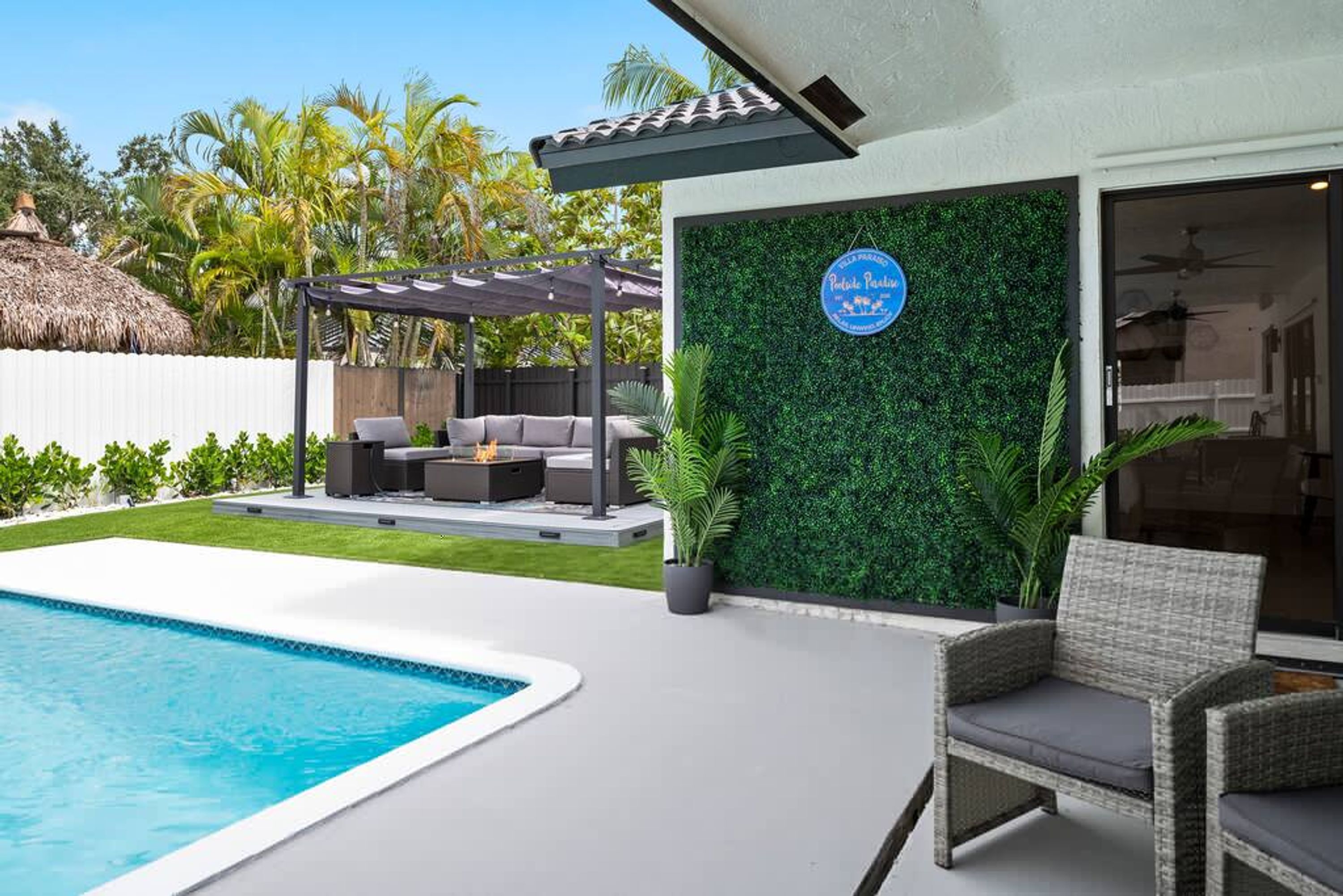 Un espace piscine extérieur moderne, doté d’une pergola, de sièges et d’un mur végétal orné d’un logo.
