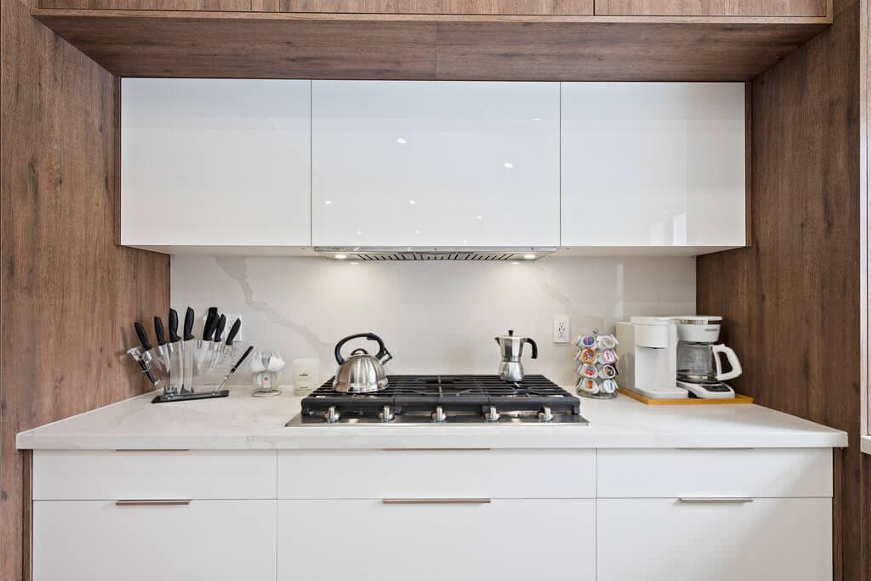A modern kitchen with white cabinets, a gas stove, a kettle, and a coffee maker.