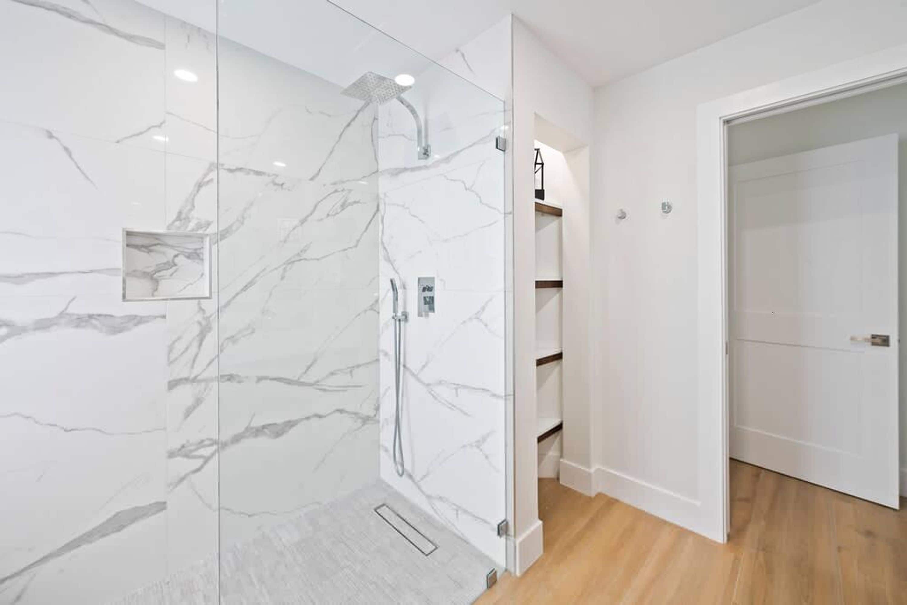 A modern bathroom with a glass-enclosed shower, marble walls, and wooden flooring.