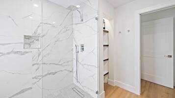 A modern bathroom with a glass-enclosed shower, marble walls, and wooden flooring.