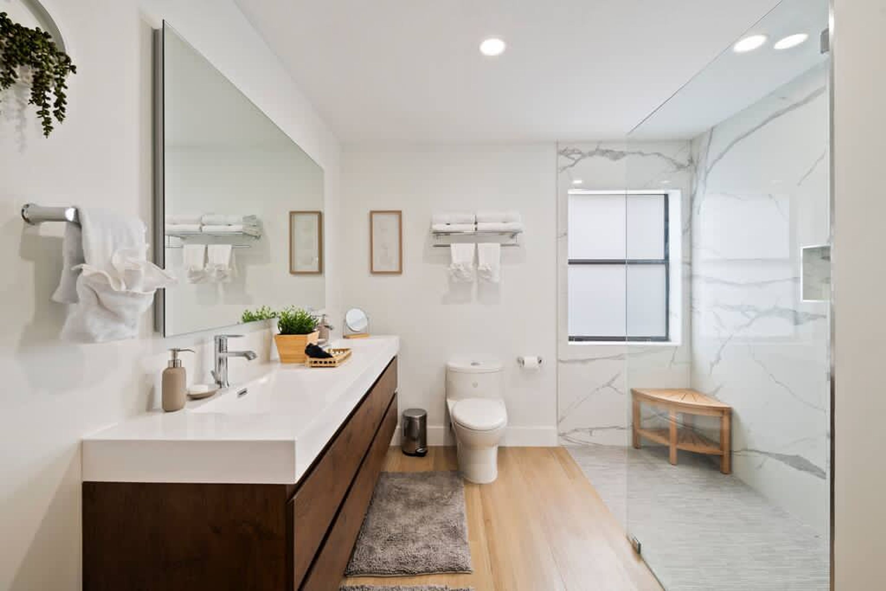 Een moderne badkamer met een wit wastafelmeubel, een grote spiegel, een toilet en een douchegedeelte.