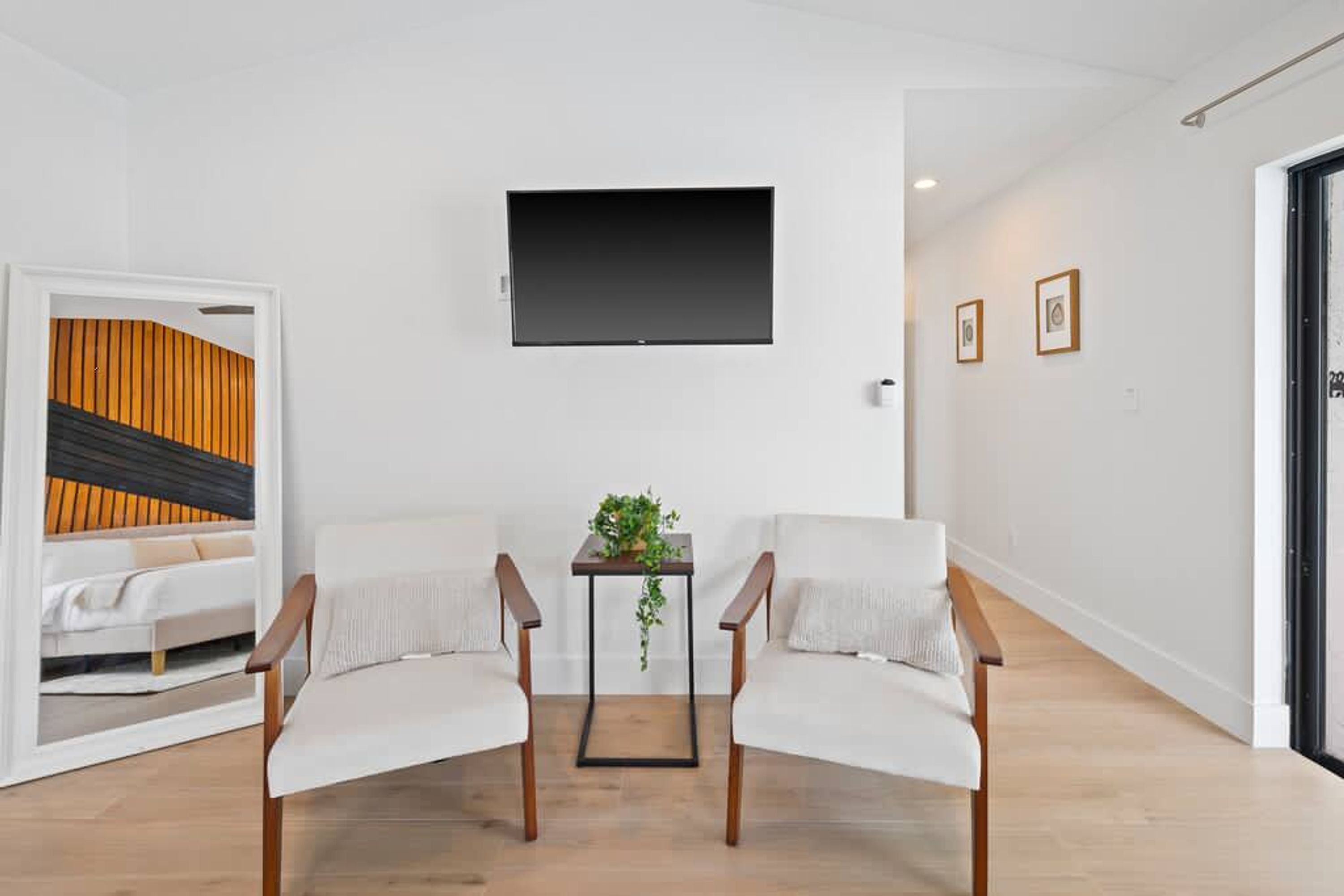 Un salon moderne avec un canapé blanc, une petite table sur laquelle est posée une plante et un téléviseur fixé au mur.