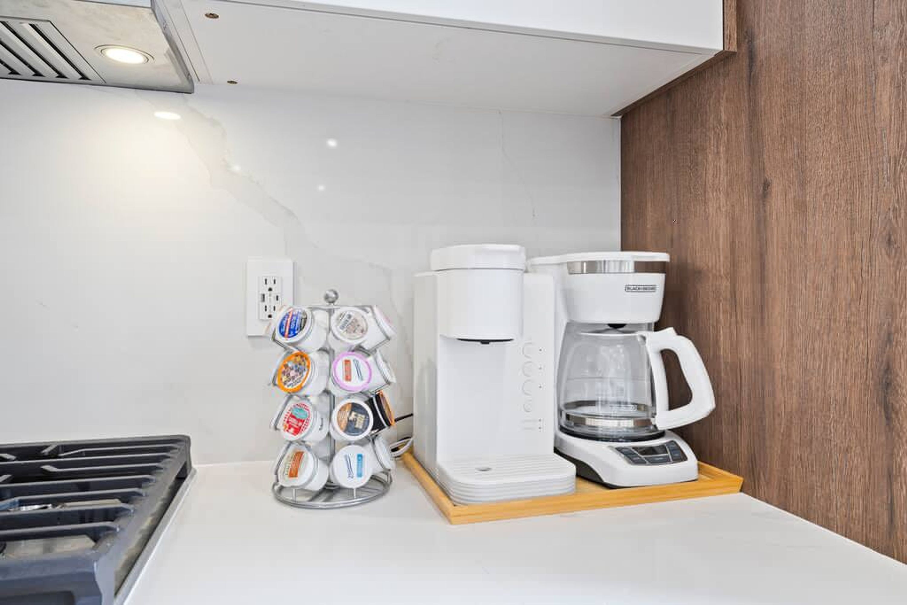 A kitchenette with a coffee maker, a coffee pod holder, and a stove.