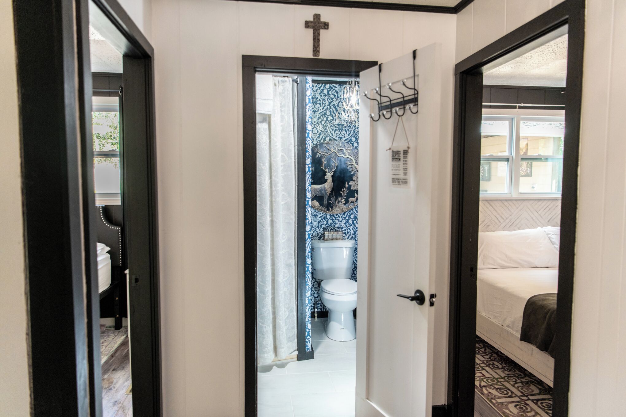 A hallway leading to a bathroom with a toilet, a shower, and a bed with a white headboard.