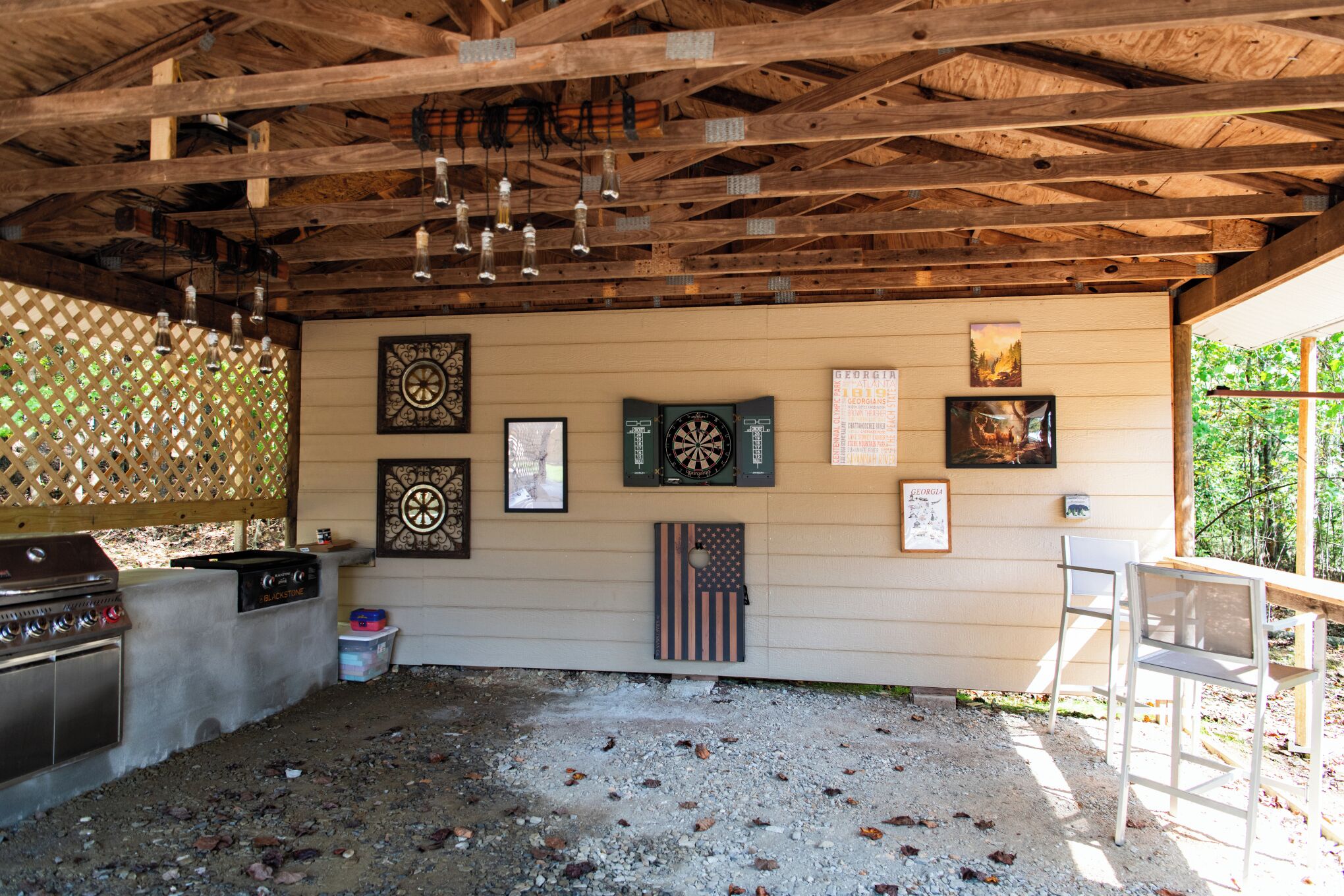 An outdoor patio area with a wooden ceiling, a grill, and various decorations including framed pictures and a dartboard.