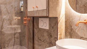 Un baño moderno con ducha de vidrio, inodoro blanco y lavamanos redondo.