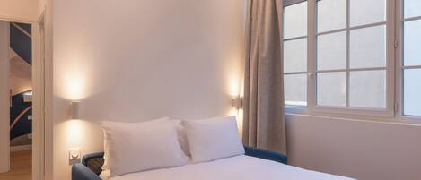A bedroom with a bed, two bedside lamps, a window with curtains, and a staircase in the background.
