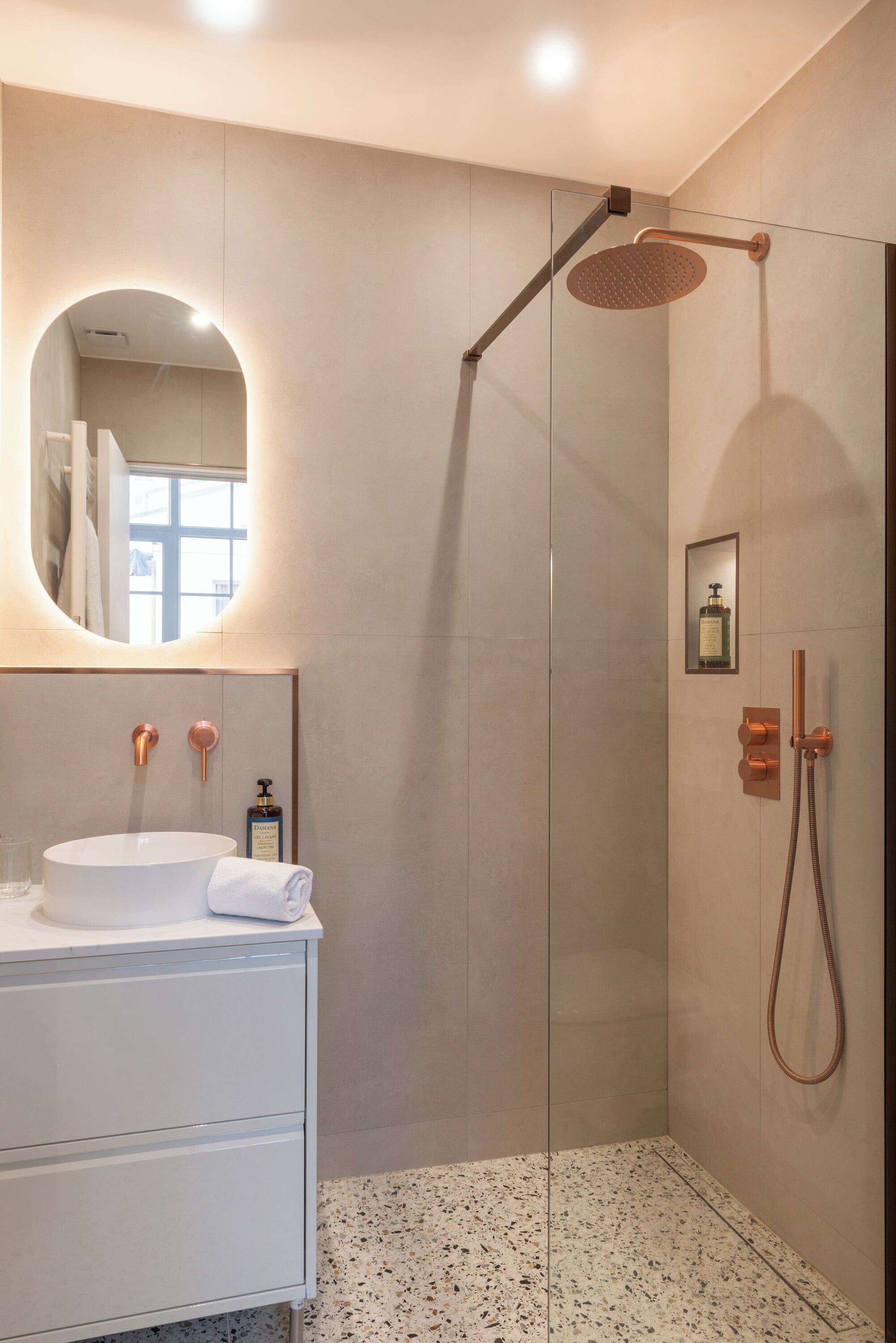 A modern bathroom with a glass-enclosed shower, a white sink with a round mirror, and a small framed picture on the wall.