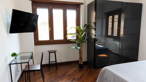 A modern bedroom with a bed, a TV mounted on the wall, a small table with a chair, a potted plant, and a window with wooden shutters. - New apartment in Rome Trastevere w/ 2 beds, living, excellent transport (Roma)