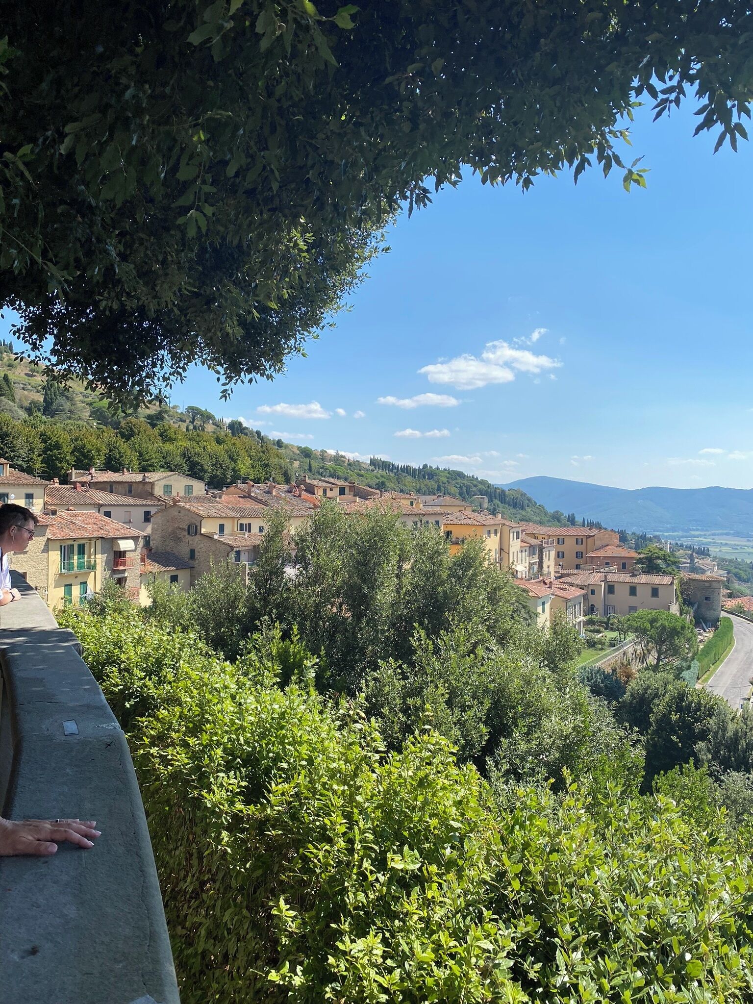 Un village perché sur une colline, avec des bâtiments traditionnels, un mur de pierre et une végétation luxuriante.