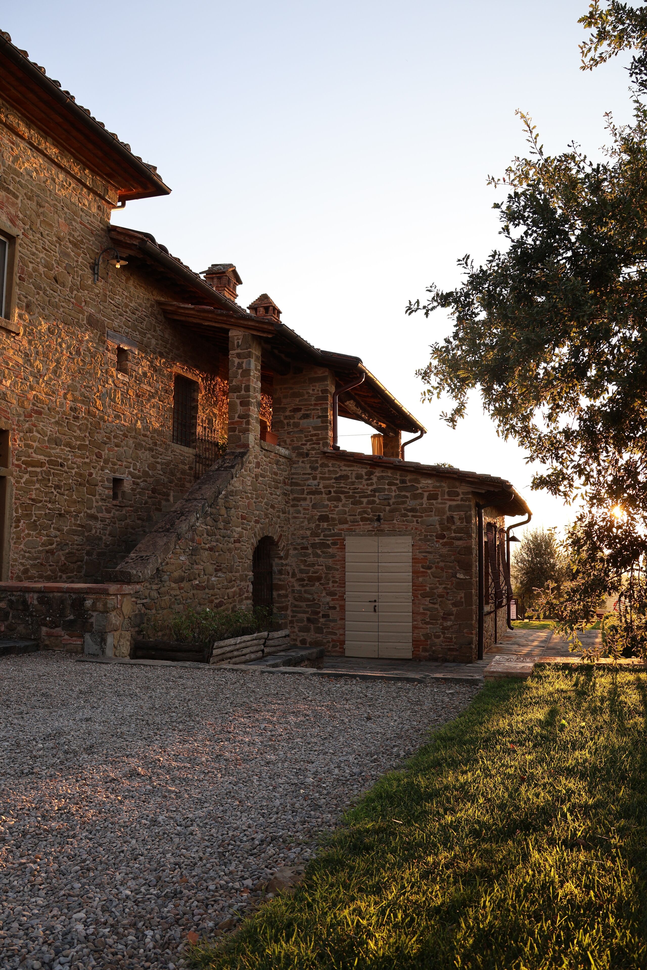 A stone building with a staircase leading to a wooden door, surrounded by gravel and grass.