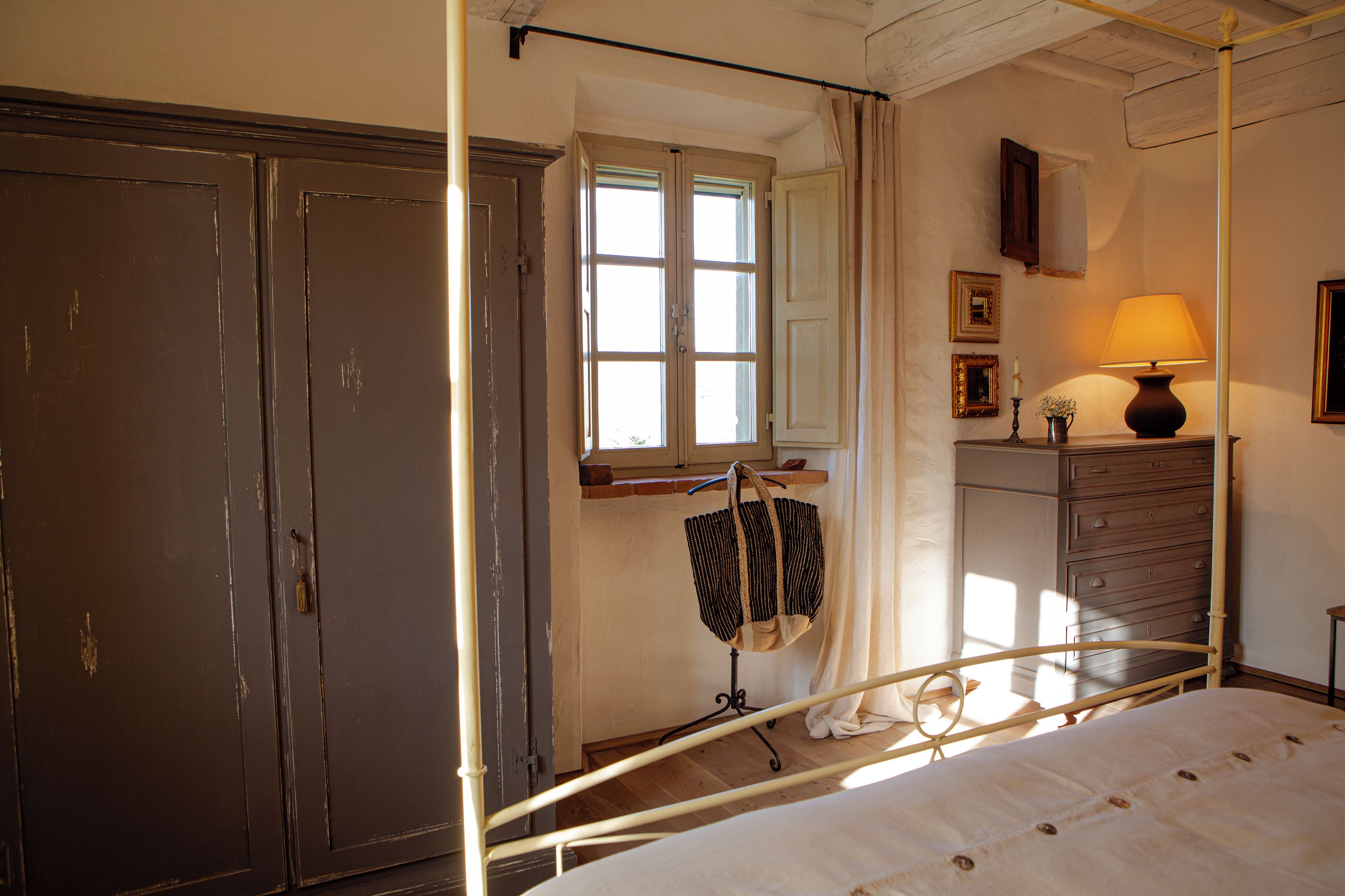 Un dormitorio con cama con dosel, cómoda de madera, espejo y ventana con cortinas.