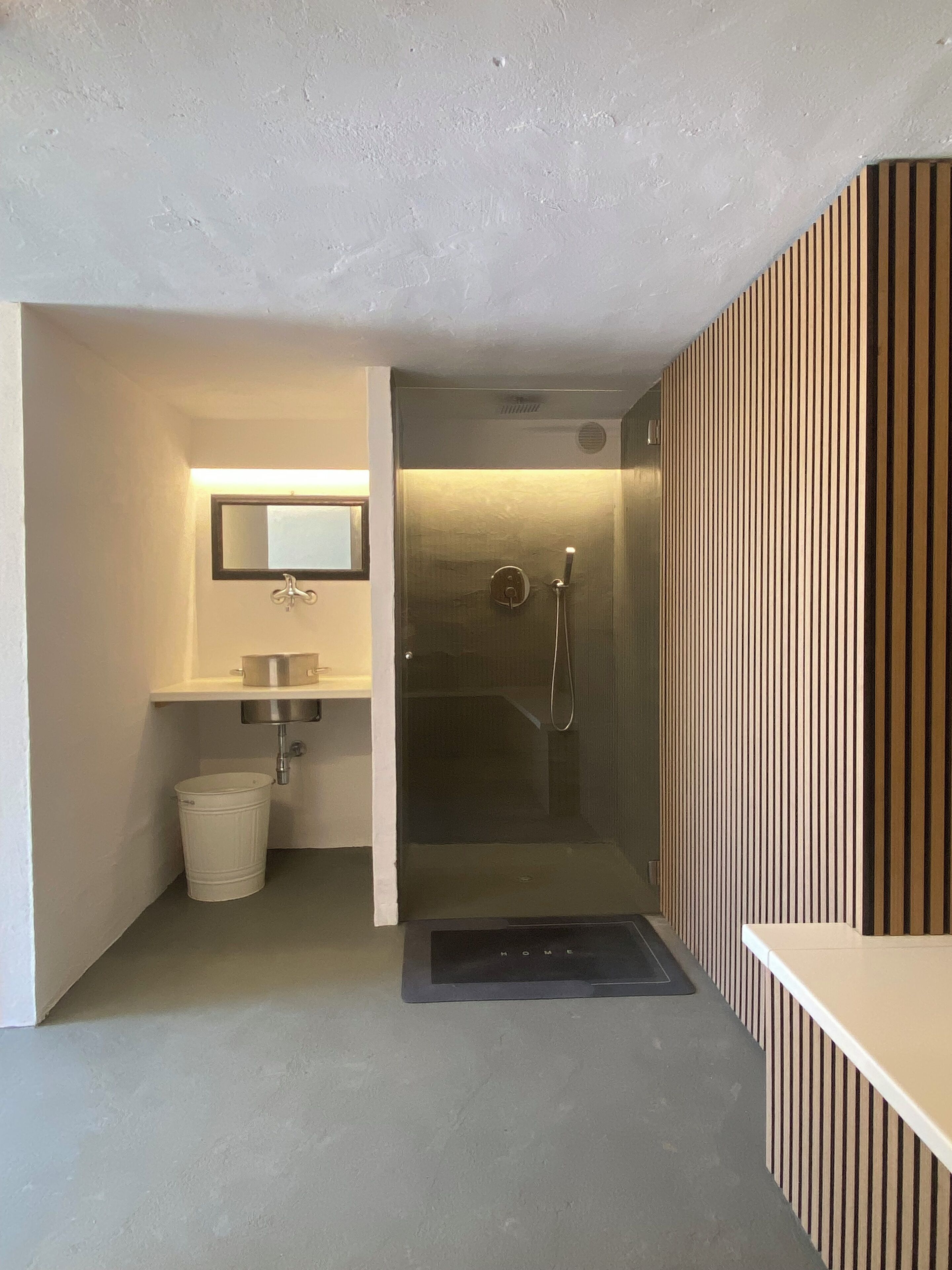 A modern bathroom with a glass shower enclosure, a sink with a mirror, and a trash bin.