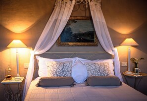 A bed with a canopy, two bedside lamps, a framed painting, and a small table with a vase. - Podere Cavalbianco (Monte San Savino)