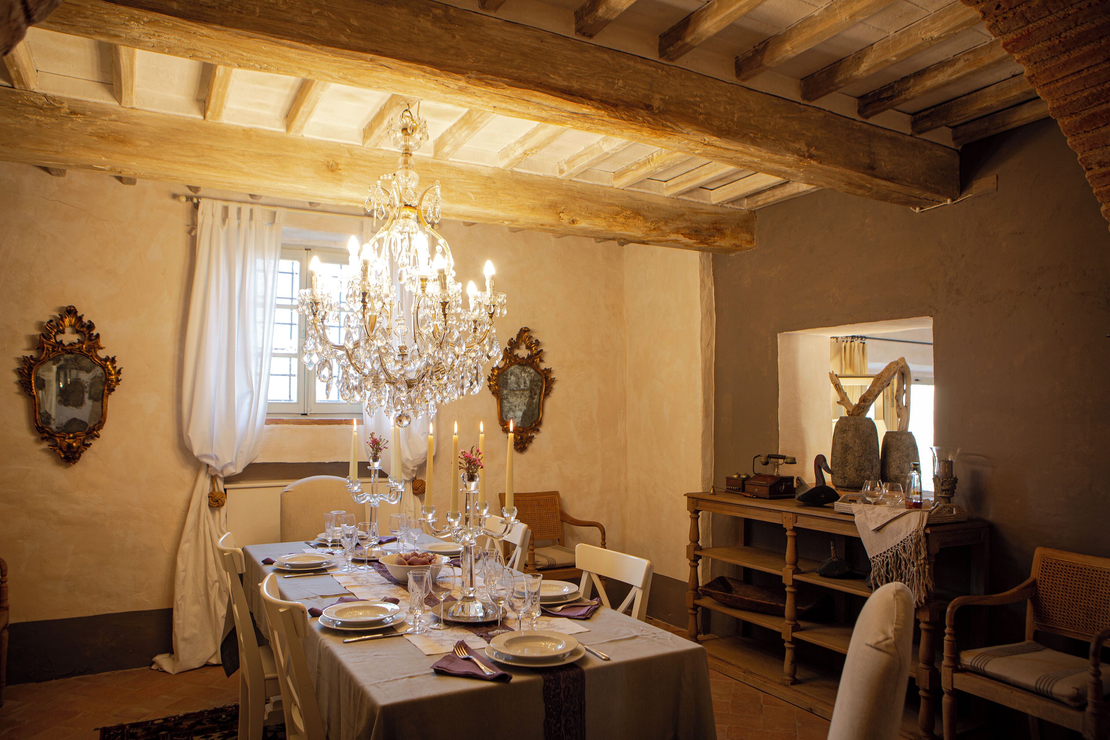 A dining room with a chandelier, wooden beams, and a table set for a meal.