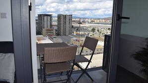 Un balcone con sedie in vimini e vista su un paesaggio urbano, con palazzi alti e un aeroporto in lontananza.