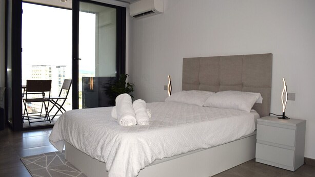 Una camera da letto moderna con un letto grande, un comodino e una poltrona vicino alla finestra.