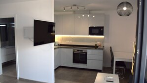 Una cucina moderna con mobili bianchi, forno integrato e microonde. È presente un'area pranzo con tavolo e sedie bianche.