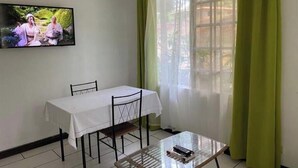 A room with a dining table, chairs, a glass coffee table, a TV on the wall, and green curtains. - Rupia Apartment.

 (San Pedro Town)