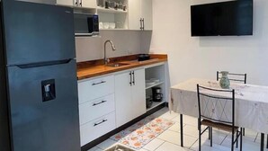 A compact kitchen with a refrigerator, microwave, sink, and white cabinets. There's a dining table with chairs and a flat-screen TV mounted on the wall. - Rupia Apartment.

 (San Pedro Town)