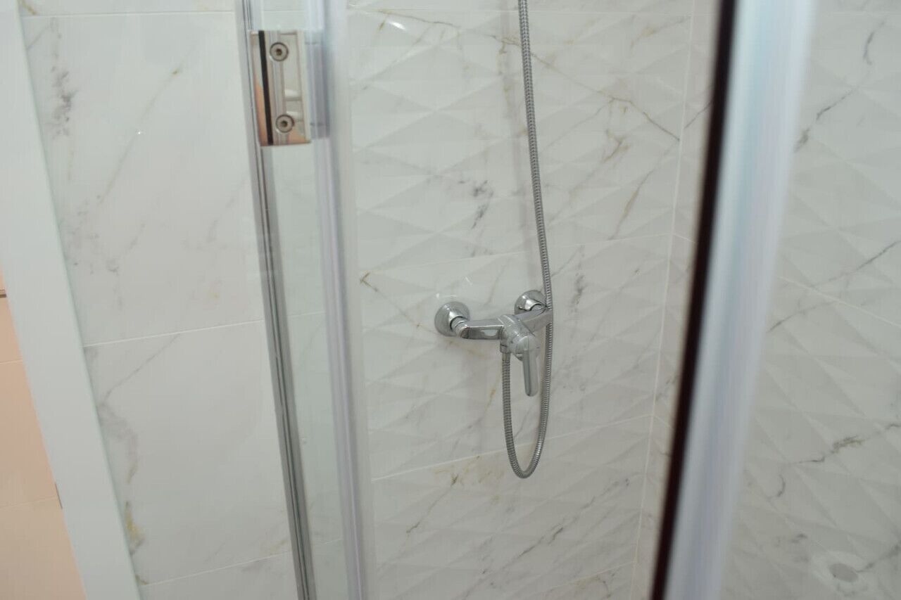 Une douche fermée par des parois en verre, dotée d’un pommeau de douche à main et d’un panneau de commande fixé au mur.