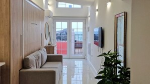 Un salon moderne avec un canapé, un téléviseur fixé au mur et une grande fenêtre donnant sur la mer.
