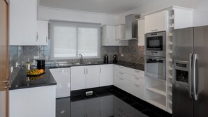 Una cocina moderna con armarios blancos, encimera negra, refrigerador de acero inoxidable y horno empotrado.