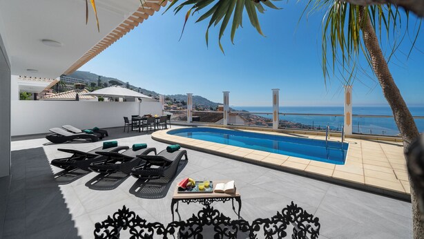 Zona de piscina en la azotea con tumbonas y una mesa con frutas y un libro.