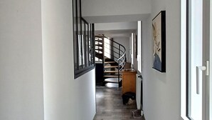 Käytävän lattia on puuta, siellä on matto, seinillä on kehystettyjä tauluja ja kauempana näkyy portaikko.