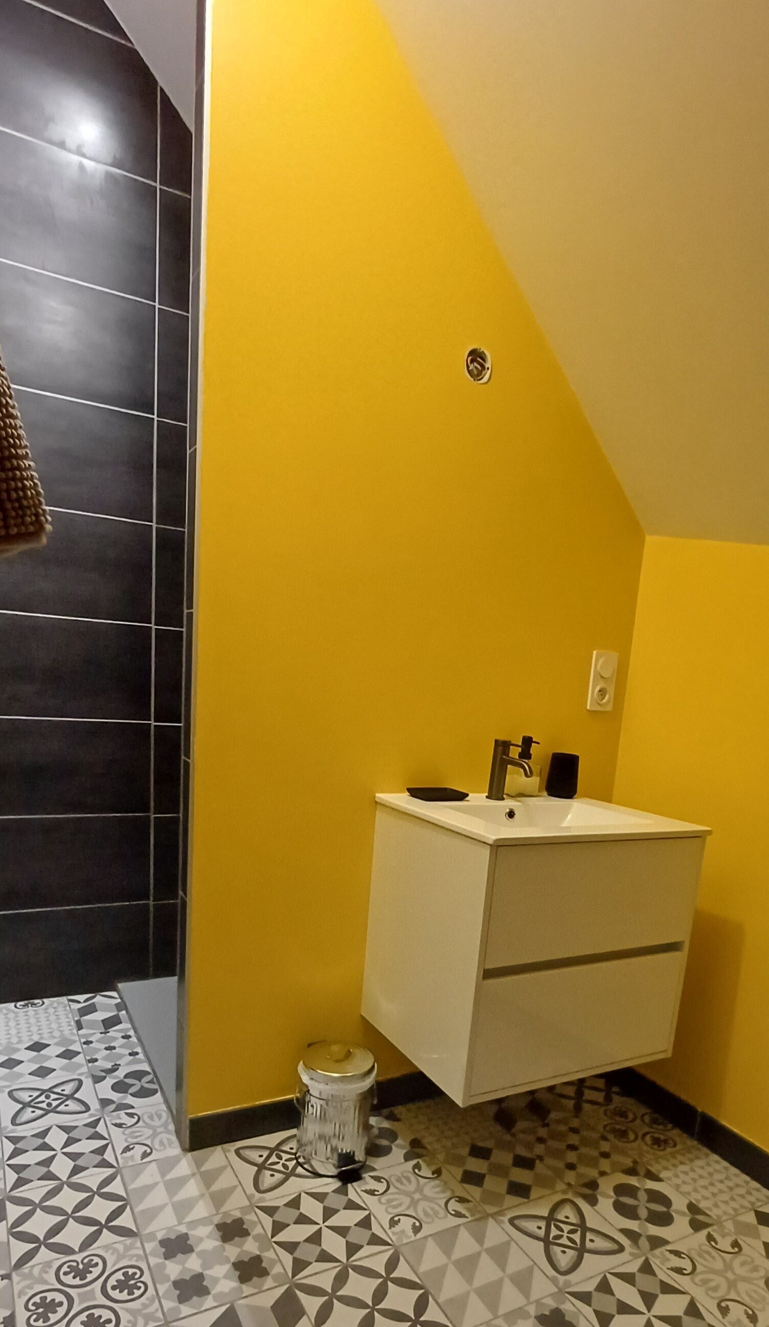 Ein Badezimmer mit gelben Wänden, einem weißen Waschbecken und Fliesenboden mit Muster.