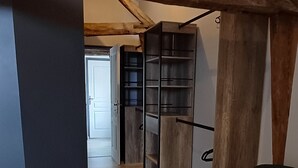 Huone, jossa on kalteva katto, näkyvillä olevat puupalkit, kuviollinen päiväpeite, musta tuoli ja seinään integroitu hyllykkö.