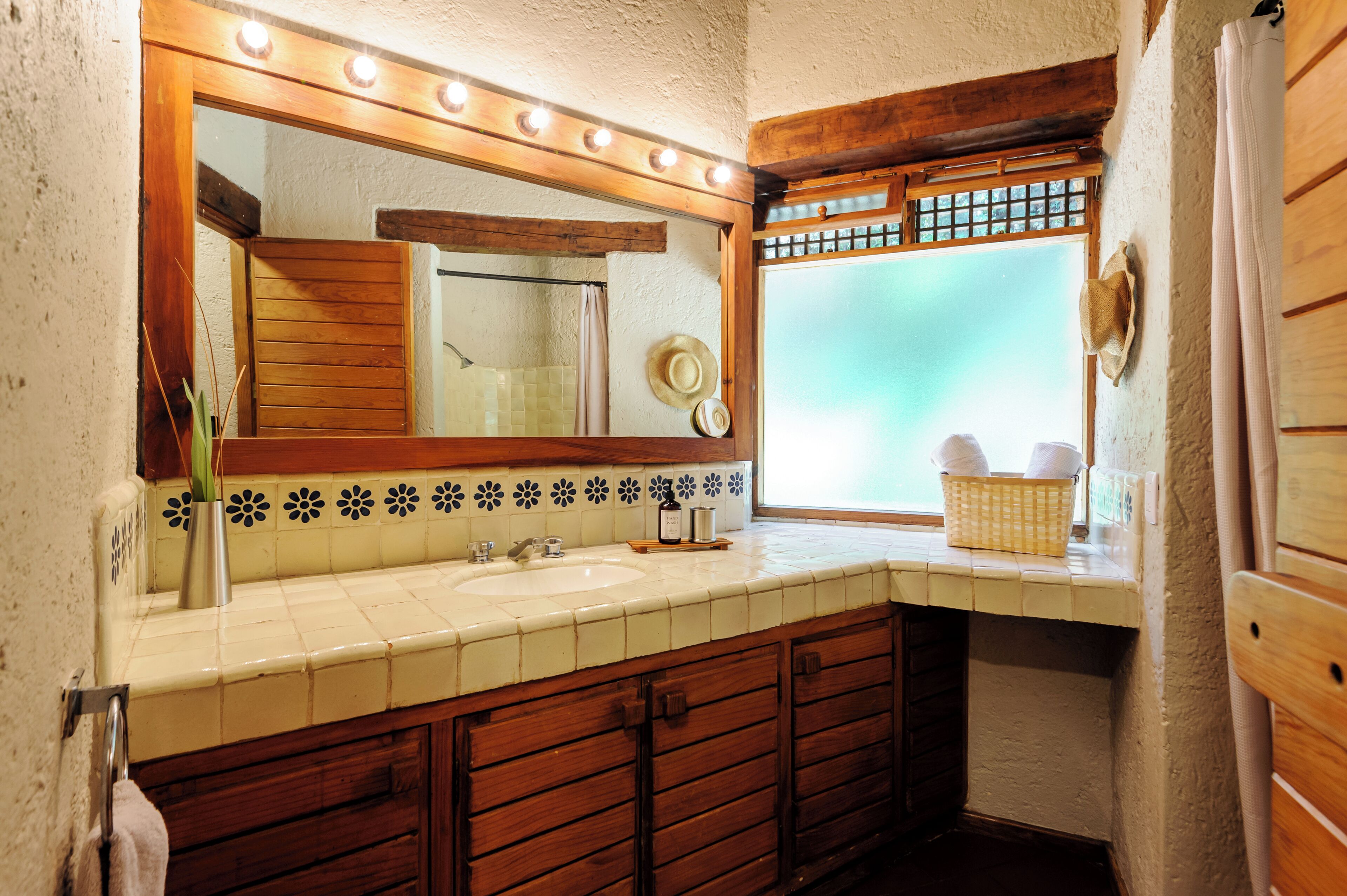 A bathroom with a wooden vanity, two sinks, a large mirror with lights, and a window with a view.