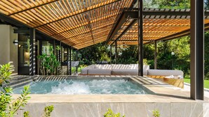 Een wellnessruimte met een jacuzzi, een houten pergola en een zithoek met kussens.