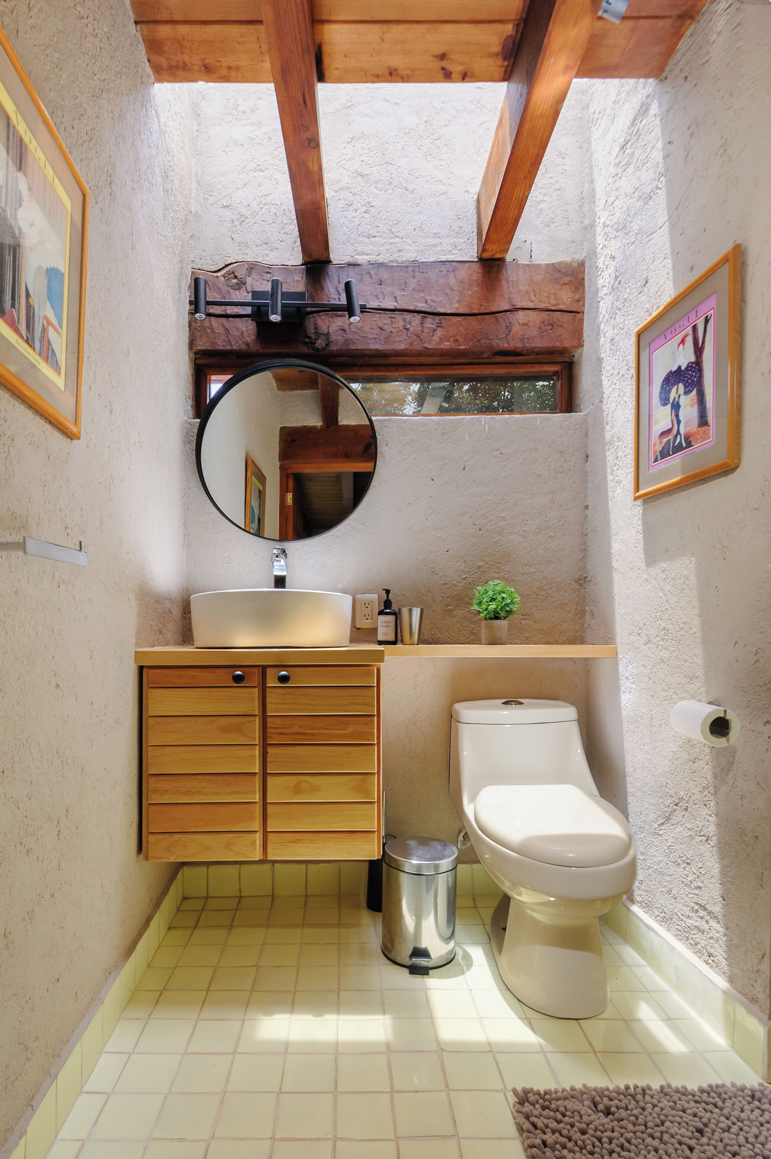 Ein kleines Badezimmer mit einem Holzbettchen, einem runden Spiegel, einer Toilette und einem kleinen Topfpflanzen.