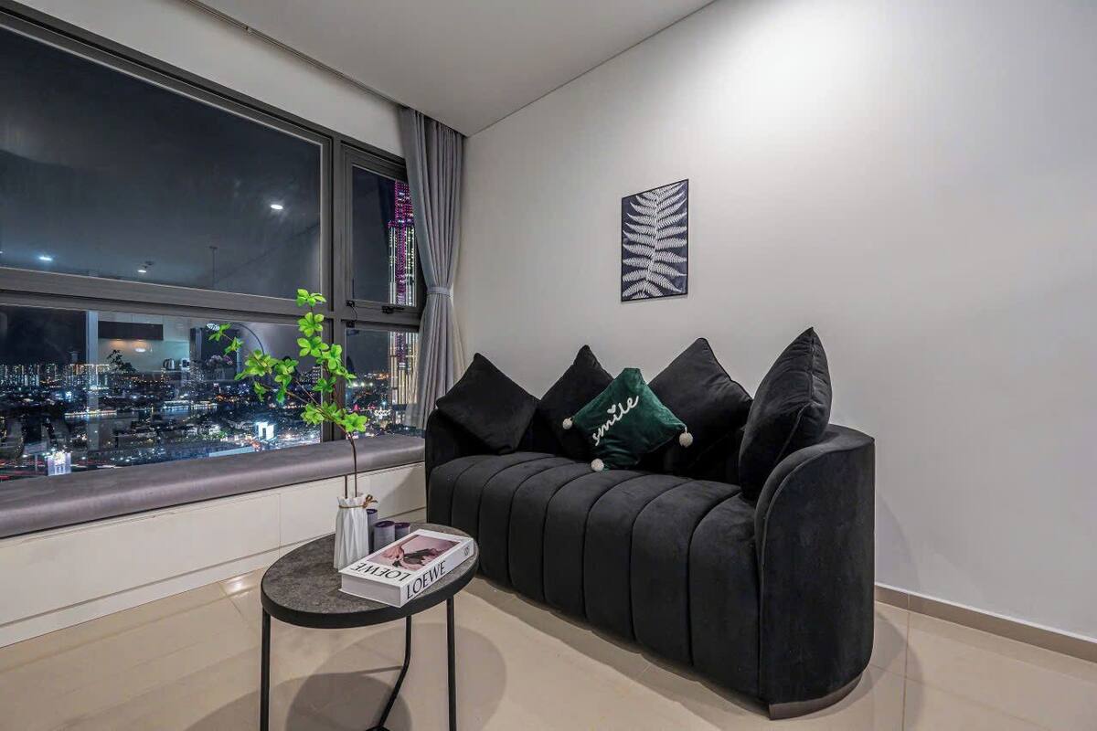 A modern living room with a black sofa, a small table with a book, and a window overlooking a cityscape.