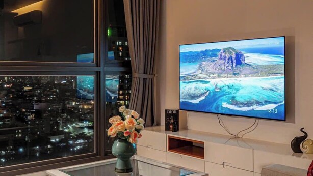 A modern living room with a large TV displaying a scenic view, a glass coffee table, and a decorative vase.
