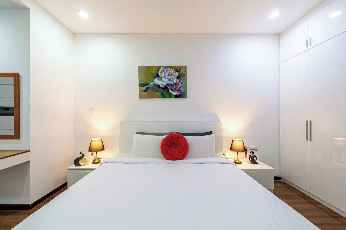 A modern bedroom with a large bed, two bedside tables with lamps, a painting on the wall, and a wardrobe.