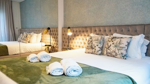 A hotel room with two beds, a green bedspread, rolled towels, a tufted headboard, and a bedside lamp. - N&N Home Porto, your home in the center of Porto.  (Porto)